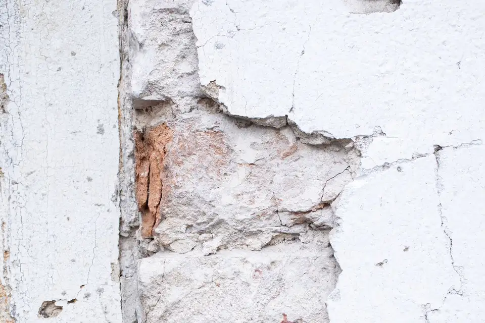 Cracked plaster wall with damaged brick underneath